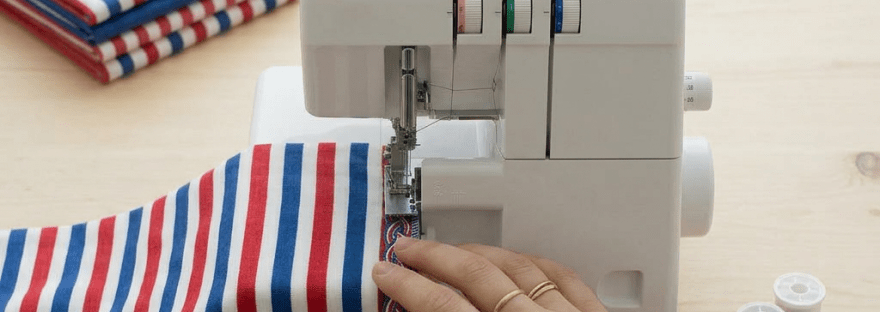 Hands untangling threads from a serger and sewing striped fabric with decorative braid trim