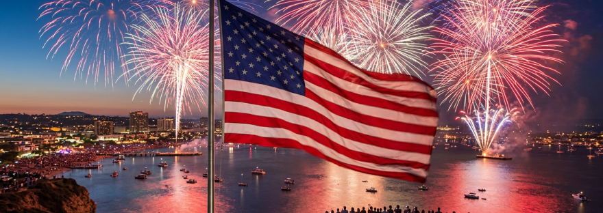 American flag waving with fireworks over waterfront and crowd at dusk