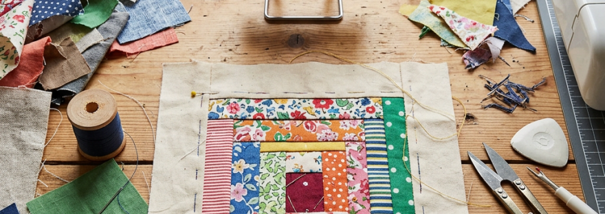 Colorful patchwork quilt block surrounded by sewing tools and fabric scraps